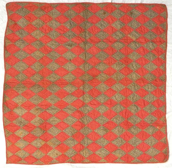 Crib quilt in patchwork diamond pattern, alternating between a light print on red cotton and a …